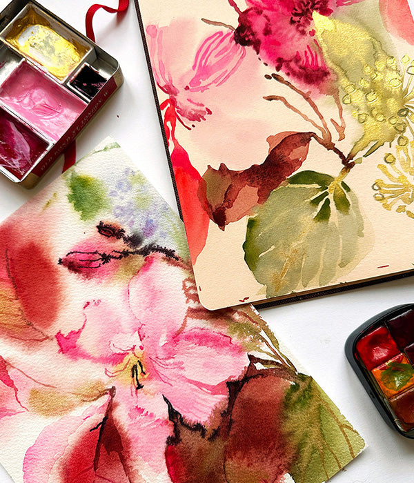 Floral watercolor painting on paper with a small paint palette and watercolor bottles.