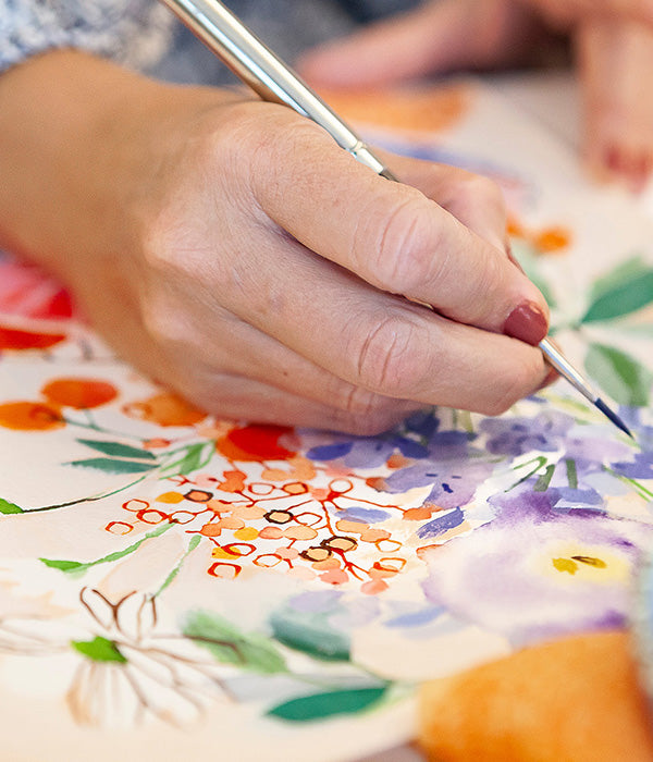 Hand holding a paintbrush over a floral painting