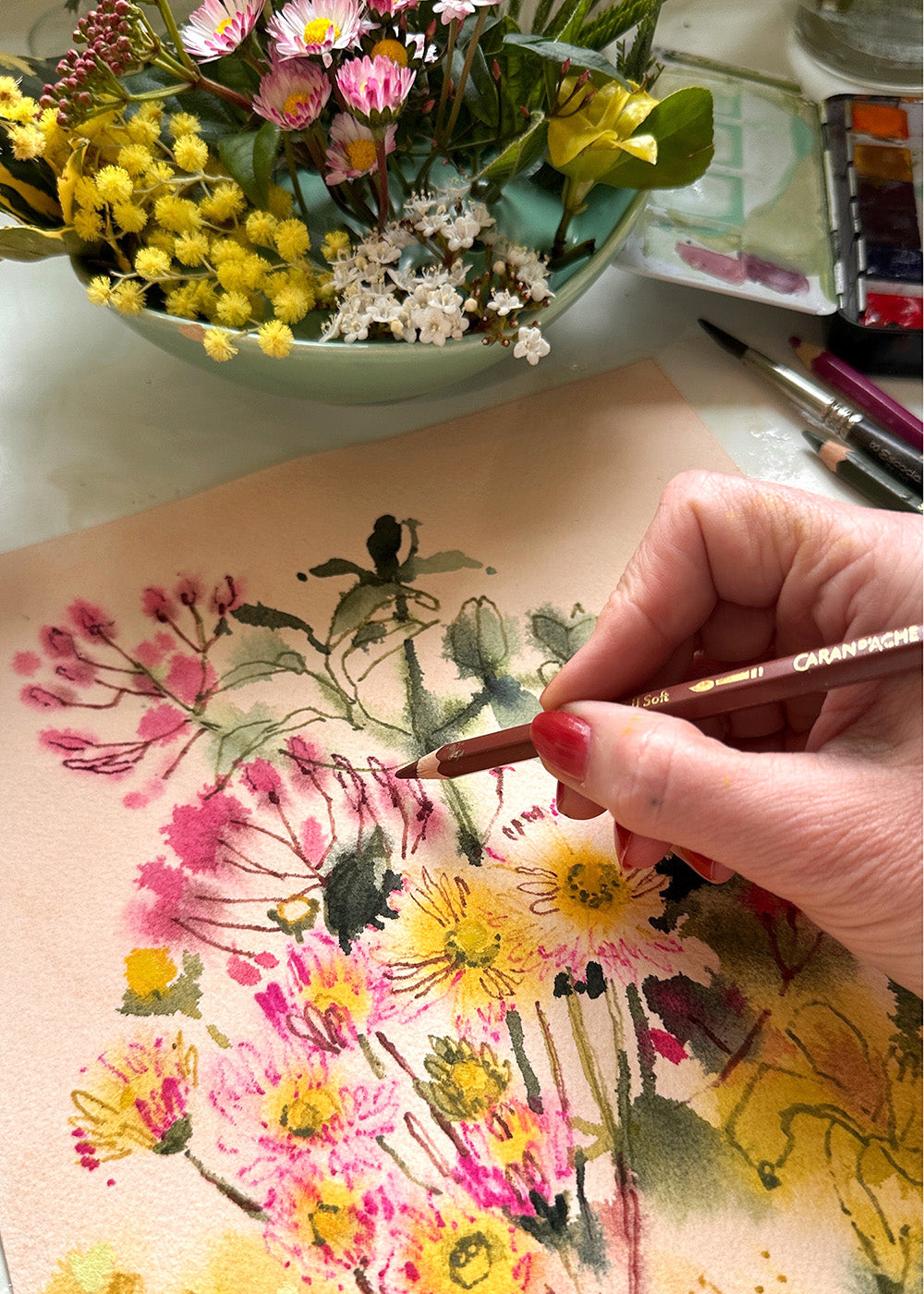 Person painting flowers on paper with a bowl of flowers in the background